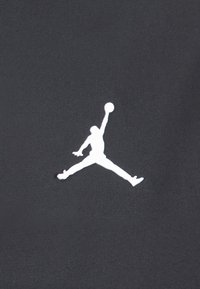 Tissu noir présentant un grand logo Jumpman blanc, représentant une silhouette de figure sautant avec un ballon de basket. Texture lisse, design minimaliste.
