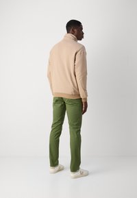 Beige high-collared sweatshirt, green trousers, white sneakers with a tan accent. Smooth texture and fitted design, viewed from the back.