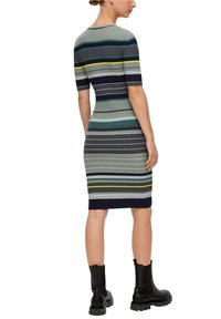 Gestreiftes Strickkleid mit kurzen Ärmeln, das vertikale und horizontale Linien in Schattierungen von Grün, Marineblau und Gelb aufweist. Getragen mit schwarzen Knöchelstiefeln.