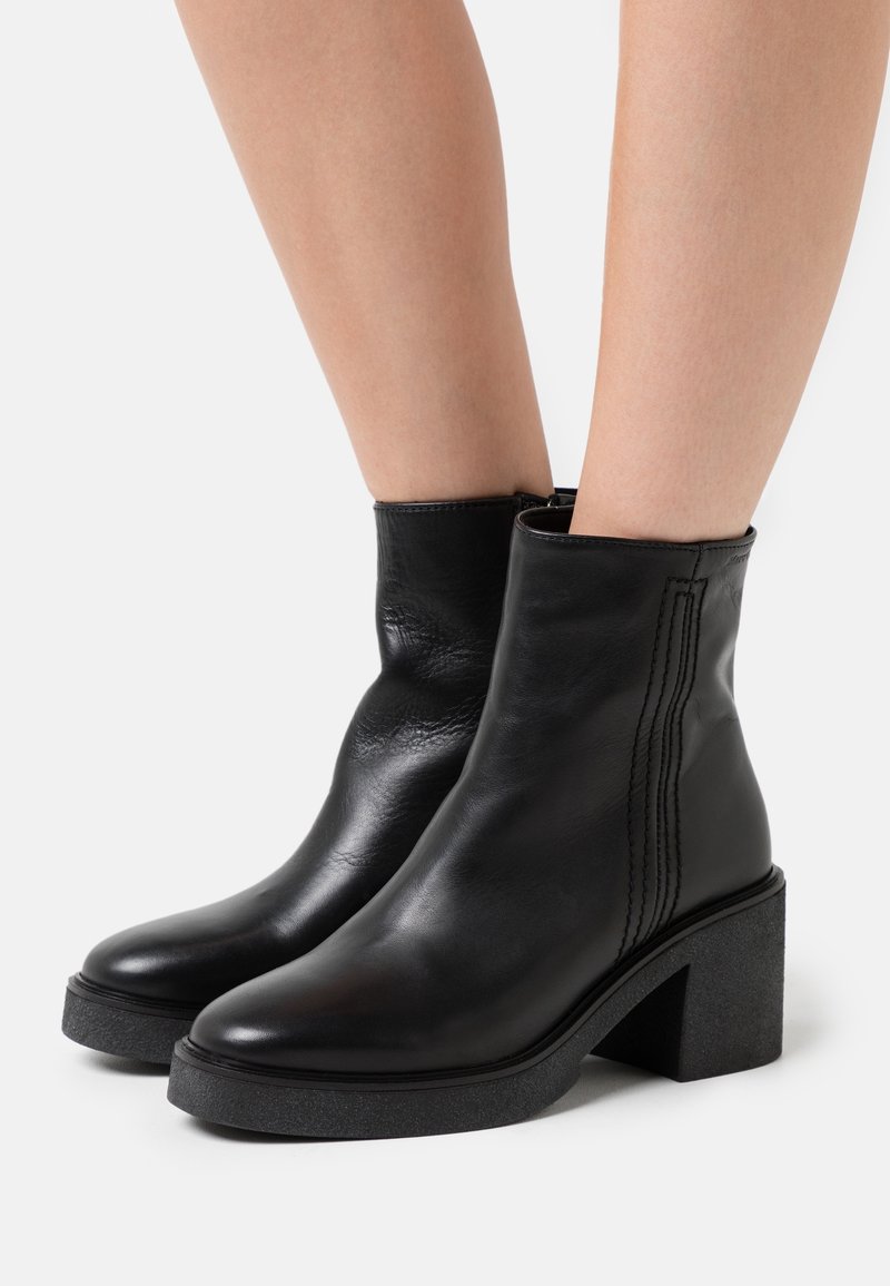 Black leather ankle boots with a square toe and thick block heel. Features vertical stitching along the sides. Smooth texture.