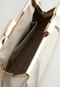 Borsa bianca con chiusura dorata, dotata di un interno beige e due tasche separate. Texture liscia con un design strutturato.