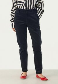 Navy corduroy trousers with a slim fit, featuring front pockets and a smooth texture. Worn with red ballet flats and a striped blouse.
