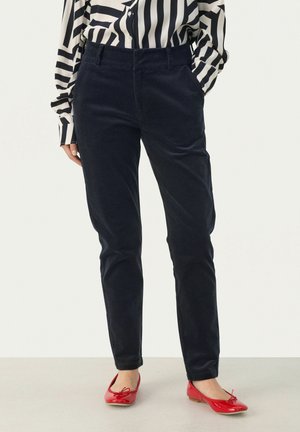 Navy corduroy trousers with a slim fit, featuring front pockets and a smooth texture. Worn with red ballet flats and a striped blouse.
