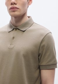 Polo bege com colarinho clássico, pala com dois botões e discreta bordadura "BOSS" no peito esquerdo, confeccionada em material de algodão suave.