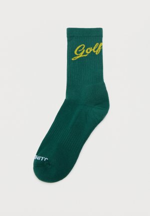Grøn besætning sok med gul "Golf" tekst nær manchet og lille hvid delvis tekst på tåen, lagt fladt på en hvid overflade.