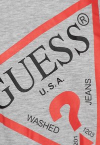 Gray cotton T-shirt featuring bold black and red text, including "GUESS U.S.A." and a triangle design with a question mark.