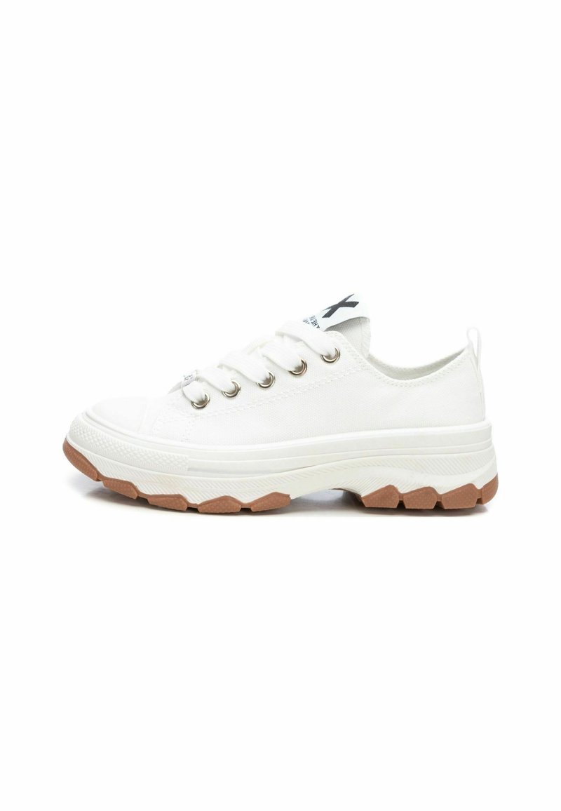 Zapatilla de lona blanca con ojales plateados, puntera de goma, suela blanca gruesa y suela exterior de goma texturizada. Detalle del logotipo negro en la lengüeta.
