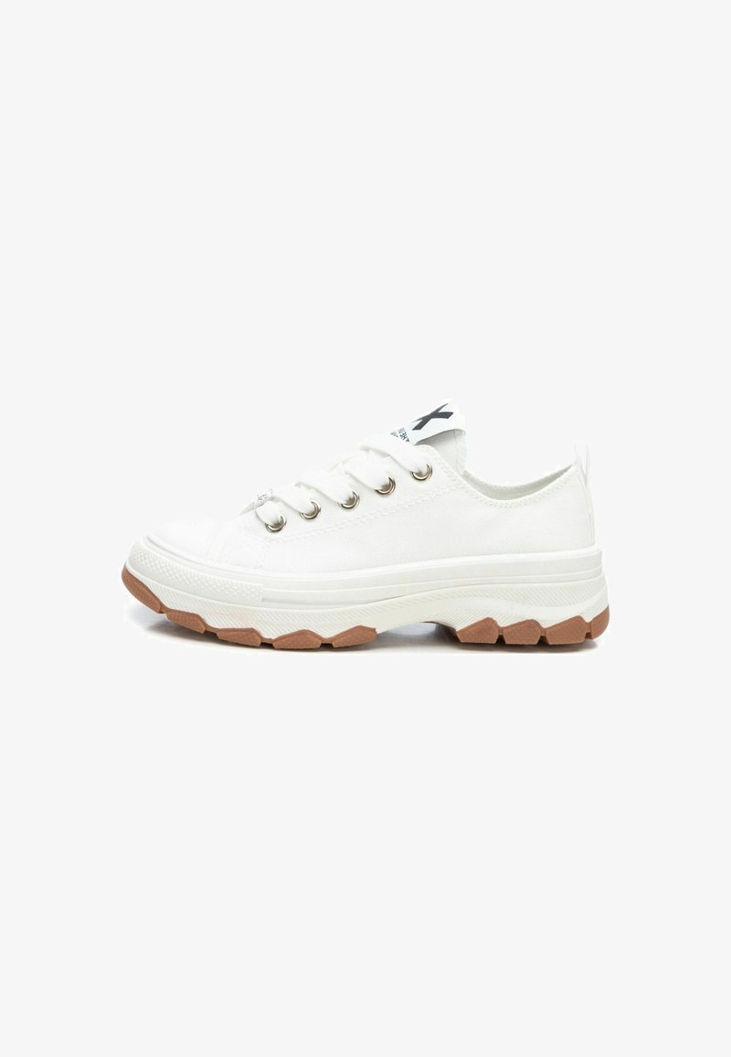 Zapatilla de lona blanca con ojales plateados, puntera de goma, suela blanca gruesa y suela exterior de goma texturizada. Detalle del logotipo negro en la lengüeta.
