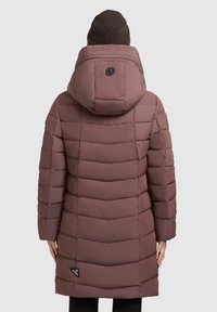 Lang mauve pufferjakke med hætte, der har vandrette quiltede sektioner og et sort logo-patch nær nederkanten. Stoffet ser glat og tykt ud.