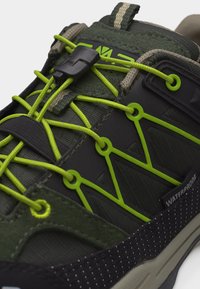 Κοντινό πλάνο πράσινου και μαύρου αδιάβροχου αθλητικού παπουτσιού με φωτεινά κίτρινα ελαστικά κορδόνια ασφαλισμένα με μαύρο κλιπ κλειδώματος.