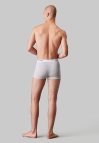 Grijs katoenen boxershorts met een aansluitend ontwerp, met een zwarte Calvin Klein-gemerkte tailleband, gezien vanuit de achterkant, blote voeten.