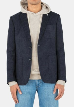 Blazer bleu marine à rayures avec deux poches avant, deux boutons et un col à cran, superposé sur un hoodie gris clair et un jean.