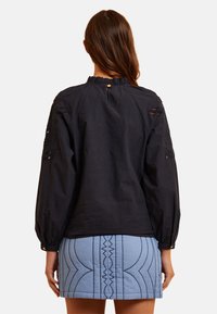 Maglietta a maniche lunghe blu navy con scollo arricciato, caratterizzata da dettagli ricamati e a intaglio sulle maniche, abbinata a una gonna trapuntata blu chiaro.