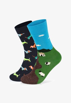 Et par sokker: den ene marineblå med farverige gravhunde, den anden blå med skyer og et grønt landskab med får og et bondehus.