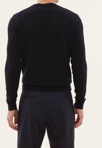 Marineblauer Rundhals-Pullover aus weichem Strickmaterial, mit gerippten Bündchen und Saum; getragen über dunklen Hosen. Schlichtes, klassisches Design.