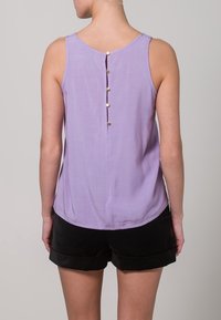 Lilac sleeveless top with a round neckline, featuring a button closure at the back and a smooth fabric texture. Paired with black shorts.