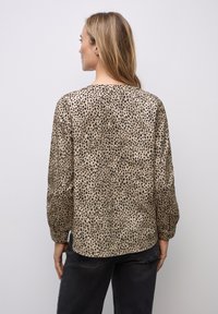 Beige bluse med sorte leopardpletter, lange ærmer, blødt stof, afrundet kant og en afslappet pasform, set fra ryggen.