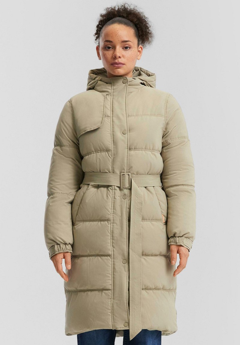 Bež dolg plašč z oblazinjenjem in kapuco, z pasom in zapiranjem na gumb; ima elastične manšete in vodoravno šivanje za dodatno teksturo.