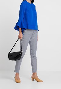 Niebieska bluzka z rozkloszowanymi rękawami, dopasowane w kratę spodnie, jasnobeżowe szpilki i czarna torebka na ramię. Czyste linie i kontrastujące tekstury.