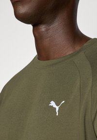 Olíva zöld, kerek nyakú póló puha anyagból, fehér Puma logóval a mellrészen és elegáns varrás részletekkel.