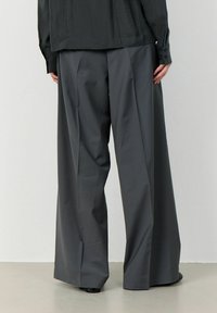 Wide-leg trousers in dark gray fabric, featuring a smooth texture and clean lines, with a relaxed fit and subtle front pleats.