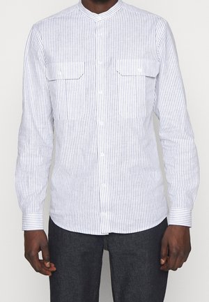 Camicia bianca a maniche lunghe con strisce verticali blu, abbottonata, con colletto alla mandarina e due tasche sul petto. Il tessuto sembra leggero e lucido.