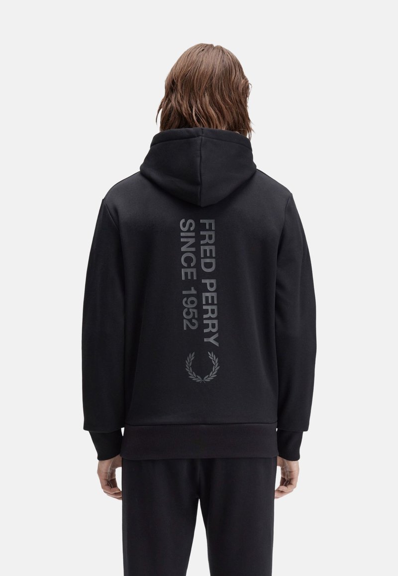 Sudadera negra con capucha, que presenta un diseño de texto gris vertical "FRED PERRY SINCE 1952" y un gráfico de una corona de laurel en la parte posterior.