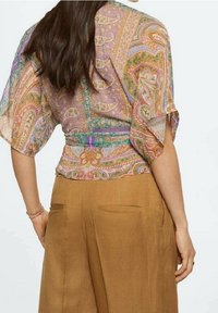 Gennemsigtig, mønstret bluse med paisley-design i pastelfarver; løs pasform, vidde ærmer; parret med lysebrune, højderede, lige bukser.