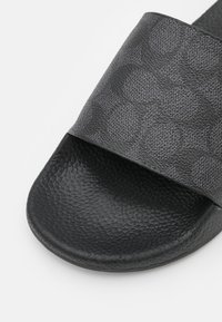 Sandale slide noire texturée avec une large bride présentant un motif circulaire subtil sur la partie supérieure.