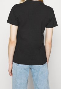 Svart bomull t-shirt med kort ärm, rund halsringning och avslappnad passform, ihopparad med ljusblå denimjeans. Bakifrån, inga framträdande detaljer.