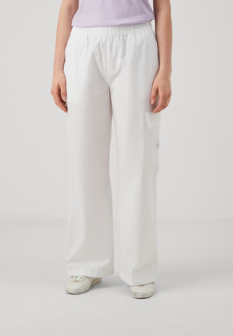 Witte wijde broek met een elastische tailleband en een cargozak aan de linkerzijde, gemaakt van gladde, lichte stof.