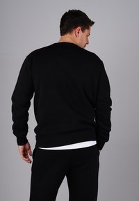 Black sweatshirt featuring a round neckline, ribbed cuffs, and hem. The fabric appears soft with a smooth texture, styled over black pants.