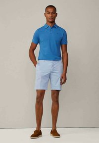 Blauwe polo met korte mouwen, gecombineerd met lichtblauwe shorts. Zachte textuur en casual pasvorm. Bruine instappers maken de look compleet.