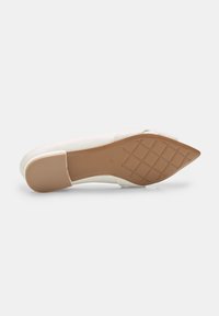 Chaussure blanche à bout pointu avec un dessus lisse ; elle présente un petit talon et une semelle en caoutchouc texturé de couleur beige avec un motif en croix.