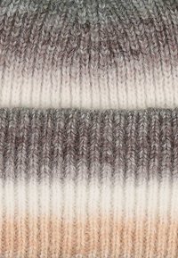Kootud müts, millel on gradient ombre muster, mis üleminekut teeb tumedast hallist heledale kreemile, ja mis on klaaritud tekstuurse soonikuga ning pehmest villast materjalist.