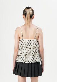 Femme avec une queue de cheval blonde portant un haut sans manches à volants blanc à pois et une jupe plissée noire, vue de dos.