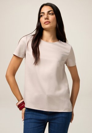 Top corto de color beige claro con una textura suave, escote redondo y un corte relajado, combinado con jeans de color azul oscuro y pulseras multicolores.