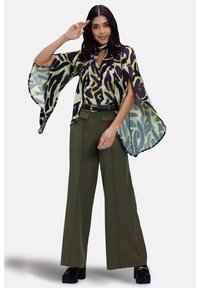 Blusa fluida a fantasia in verde chiaro e viola scuro, abbinata a pantaloni a vita alta verde oliva e scarpe platform nere chunky.