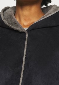 Indumento con cappuccio in suede nero, foderato in morbido pile grigio. Presenta una texture liscia e una cucitura visibile lungo l'apertura frontale.