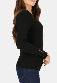 Czarny sweter z długim rękawem wykonany z prążkowanej tkaniny, charakteryzujący się dopasowanym krojem oraz złotymi guzikami na mankietach.