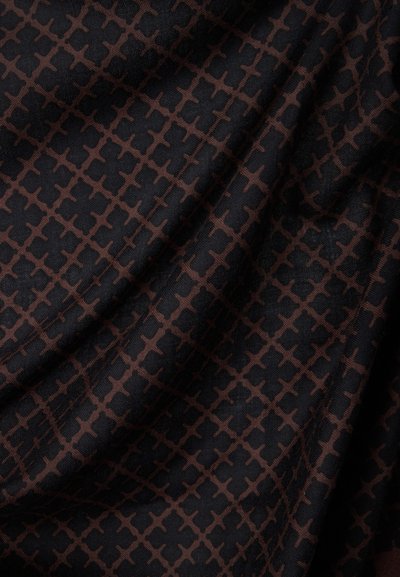 Tissu foncé avec un motif répétitif de croix brunes entrelacées, présenté avec de légers plis mettant en valeur la texture et le tombé.
