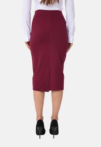 Gonna a tubino bordeaux aderente con spacco posteriore, realizzata in tessuto elastico. Abbinata a scarpe nere con tacco alto e una camicia bianca con bottoni.