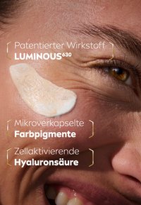 Creme auf die Haut aufgetragen, hellbeige Farbe mit einer glatten, leicht glänzenden Textur. Textüberlagerungen erwähnen patentierte Inhaltsstoffe und mikroverkapselte Pigmente.