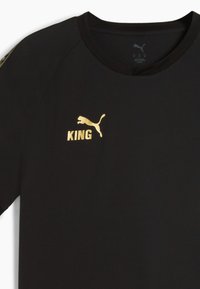 Sort atletisk skjorte med korte ærmer; har guld "KING" tekst og Puma-logo. Strukturstof med rund hals.