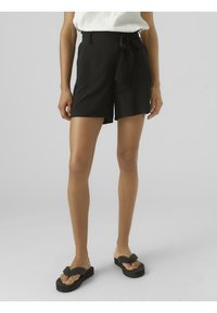 Black shorts made of lightweight fabric, featuring a high waist, tie belt, and a relaxed fit. Worn with black flip-flops.