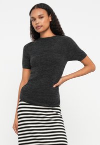 Sweater de malha ajustado em cinza escuro com mangas curtas e decote redondo, combinado com uma saia listrada em preto e branco. Textura suave, design minimalista.