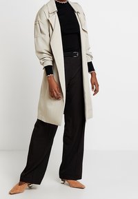 Béžový trenčkot s nadměrným střihem, dlouhými rukávy a černými akcenty. Kombinován s černými kalhotami s vysokým pasem a světlými podpatky.