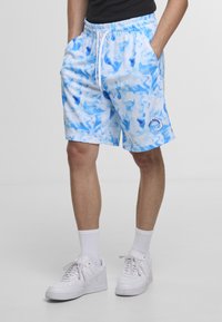 Lys blå mønstrete badeshorts med snøring i midjen og sidelommer, med en bølgelogo på leggen og kombinert med hvite joggesko.