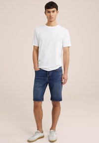 Balta marškinėlių su apvaliu iškirpimu, džinsiniai šortai su apvyniotais kraštais ir balti sportbačiai su šviesiai ruda padu. Paprastas, laisvalaikio aprangos derinys.