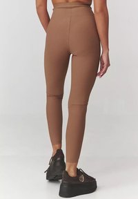 Brązowe prążkowane legginsy z wysokim stanem, charakteryzujące się gładką teksturą i dopasowanym krojem, zestawione z czarnymi sneakersami na platformie.